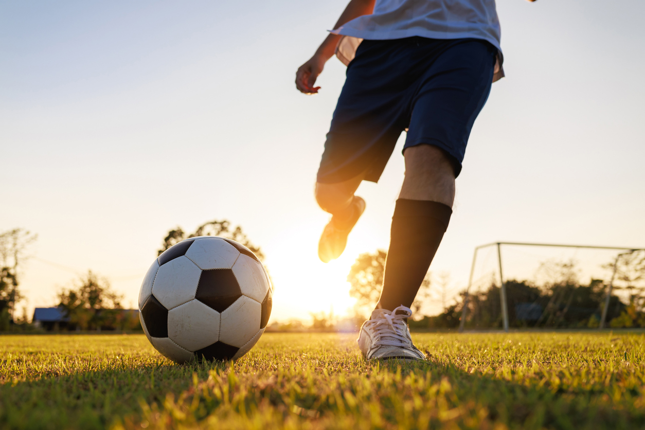 Close up shot of soccer player kicking ball. Action sport outdoors playing football for exercise at green grass field under the twilight sunset.