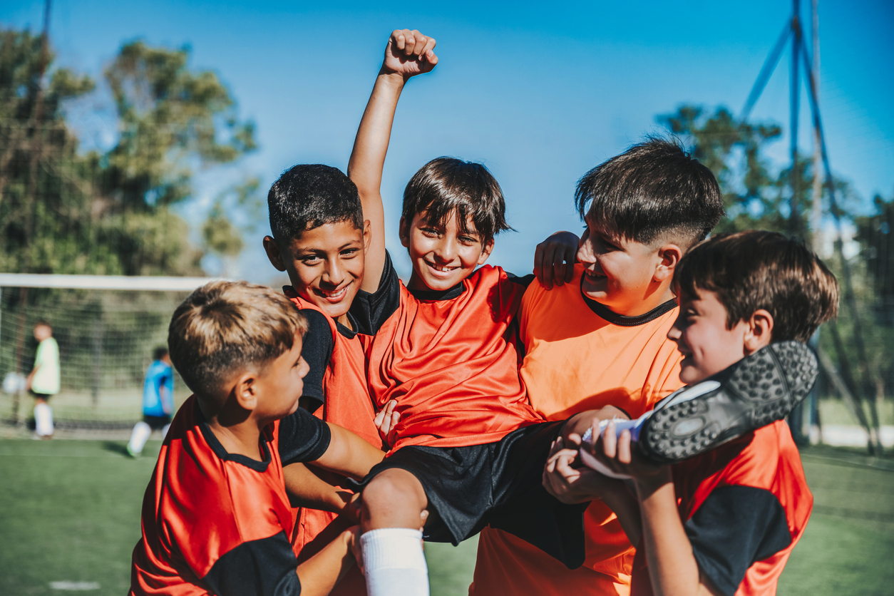 five soccer boys cheering on soccer field after scoring a goal